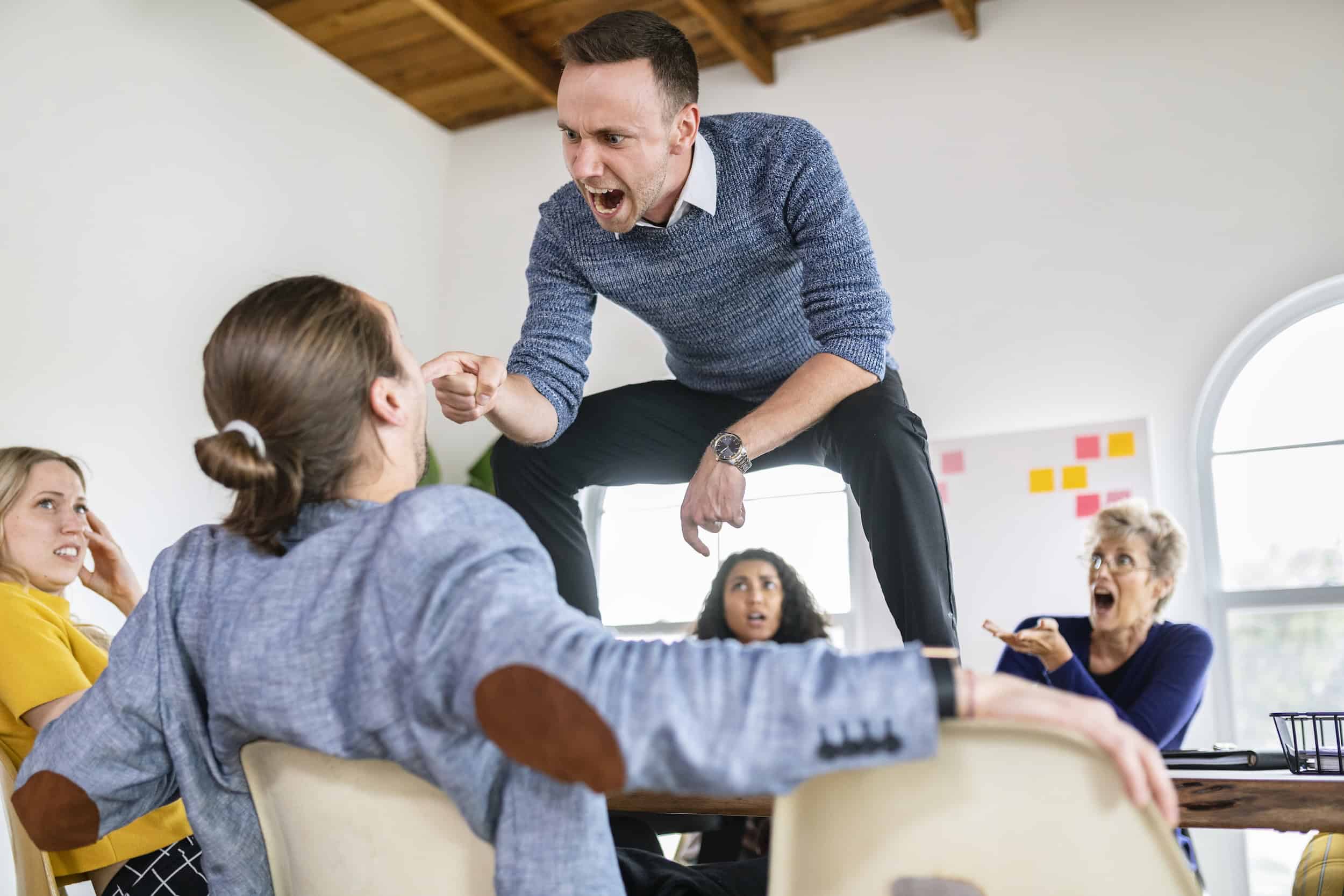 examples of verbal abuse in the workplace as an angry man is standing on table yelling at employees
